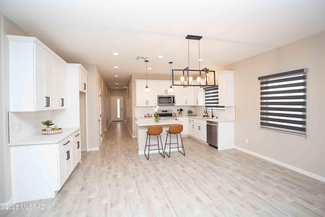 kitchen with a kitchen island, appliances with stainless steel finishes, decorative light fixtures, white cabinetry, and sink