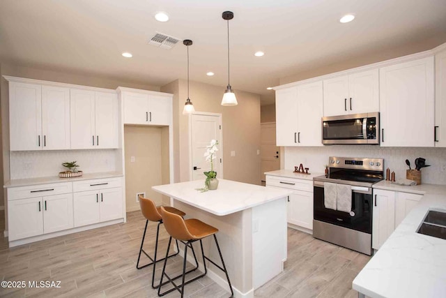 kitchen with pendant lighting, tasteful backsplash, white cabinets, a center island, and stainless steel appliances