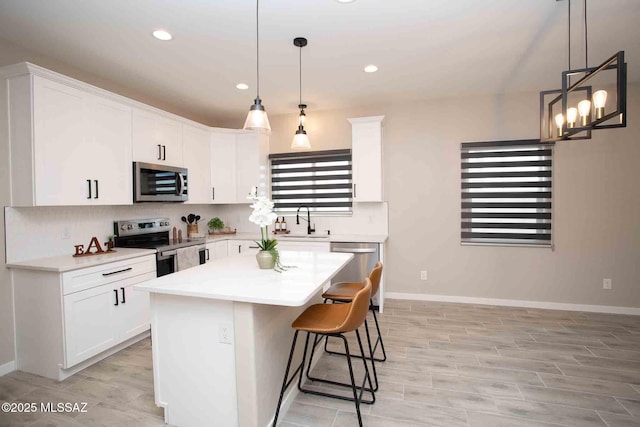 kitchen featuring a kitchen island, white cabinetry, appliances with stainless steel finishes, and hanging light fixtures