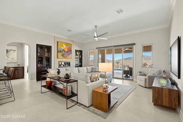 tiled living room featuring crown molding, ceiling fan, and a fireplace