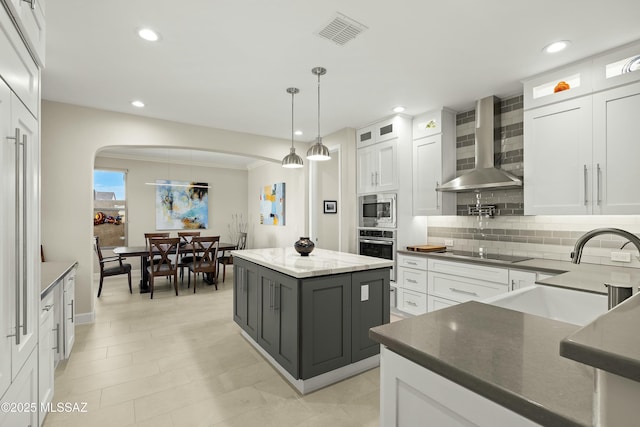 kitchen with white cabinetry, sink, a center island, stainless steel appliances, and wall chimney exhaust hood