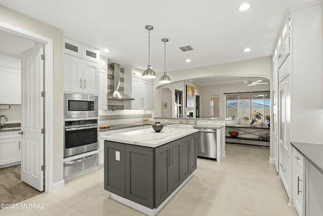 kitchen with stainless steel appliances, white cabinets, light stone counters, and wall chimney exhaust hood