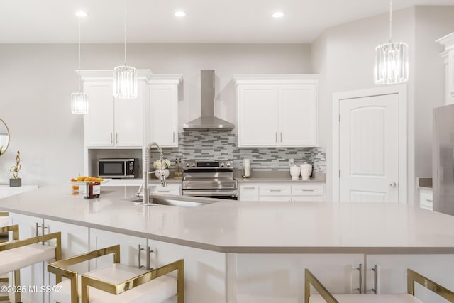 kitchen with appliances with stainless steel finishes, pendant lighting, a kitchen breakfast bar, and wall chimney exhaust hood