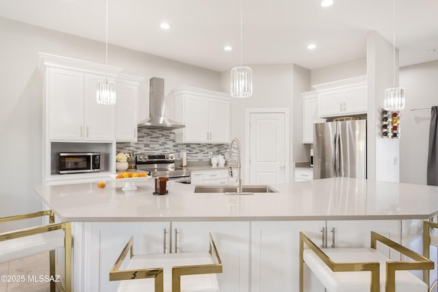 kitchen with appliances with stainless steel finishes, sink, white cabinets, hanging light fixtures, and wall chimney exhaust hood