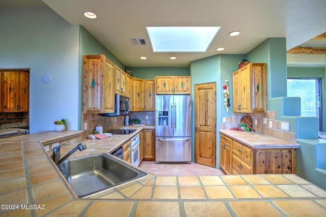 kitchen with sink, tile countertops, a skylight, stainless steel appliances, and backsplash