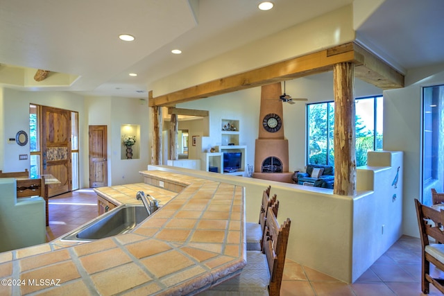 kitchen featuring sink, tile patterned flooring, a large fireplace, a kitchen island, and tile countertops