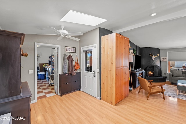 kitchen featuring ceiling fan, light wood-type flooring, vaulted ceiling with skylight, and a fireplace