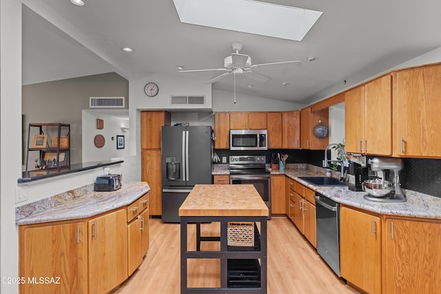 kitchen featuring sink, lofted ceiling with skylight, light hardwood / wood-style floors, and appliances with stainless steel finishes