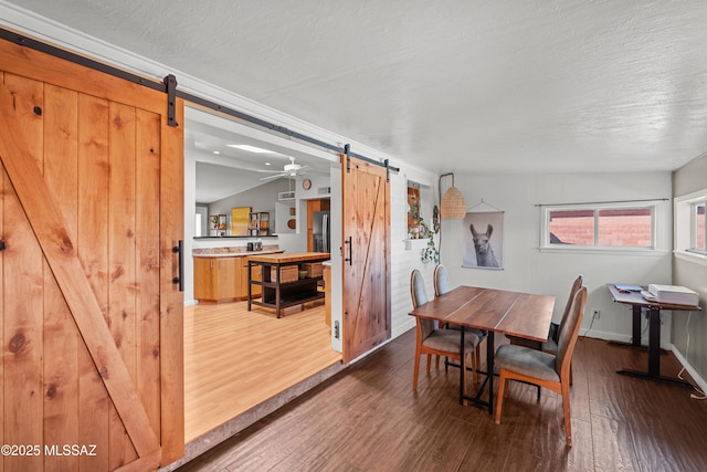 dining space with lofted ceiling, hardwood / wood-style flooring, a barn door, and a textured ceiling