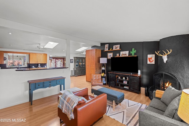 living room featuring ceiling fan, vaulted ceiling with skylight, a fireplace, and light hardwood / wood-style floors