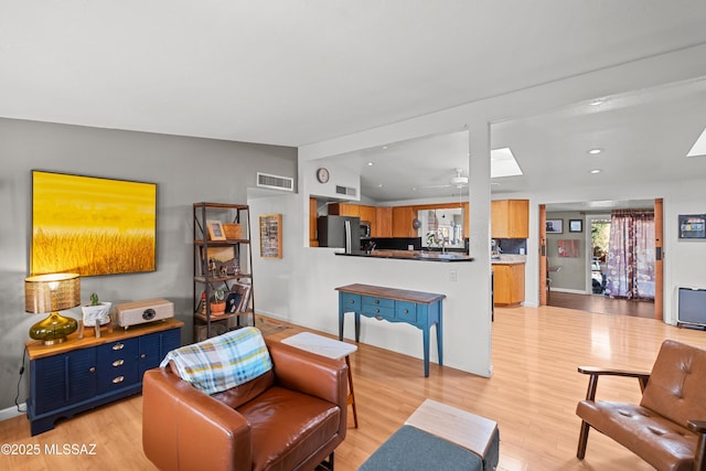 living room with ceiling fan, vaulted ceiling with skylight, and light wood-type flooring