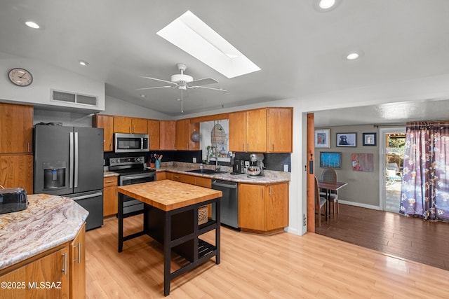 kitchen featuring sink, light wood-type flooring, ceiling fan, stainless steel appliances, and vaulted ceiling with skylight