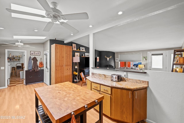 kitchen featuring lofted ceiling with skylight, kitchen peninsula, ceiling fan, and light wood-type flooring