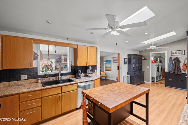 kitchen featuring lofted ceiling with skylight, sink, washer and dryer, dishwasher, and light hardwood / wood-style floors