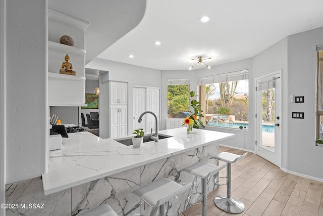 kitchen featuring sink, a breakfast bar area, light hardwood / wood-style flooring, light stone counters, and kitchen peninsula