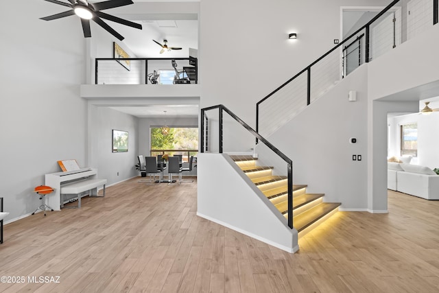 stairs with ceiling fan, wood-type flooring, and a towering ceiling