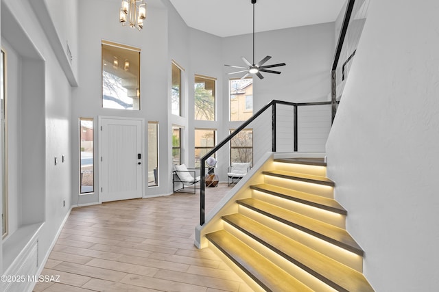 foyer featuring a towering ceiling, ceiling fan with notable chandelier, and light hardwood / wood-style floors