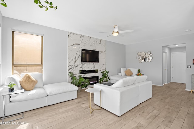 living room featuring a high end fireplace, light hardwood / wood-style floors, and ceiling fan