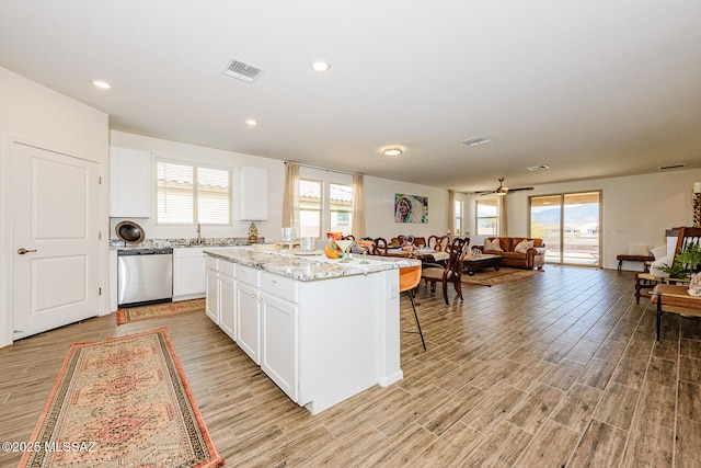 kitchen with white cabinetry, dishwasher, a center island, light stone counters, and light wood-type flooring