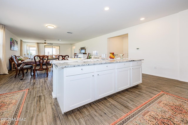 kitchen with a center island with sink, dark hardwood / wood-style floors, ceiling fan, light stone countertops, and white cabinets