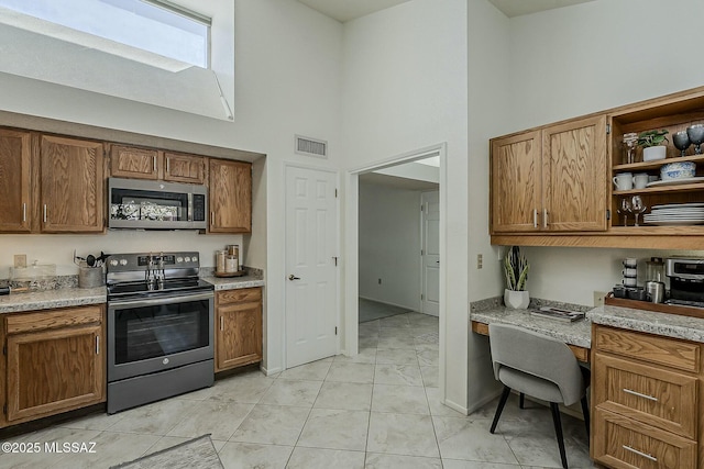 kitchen with visible vents, appliances with stainless steel finishes, a high ceiling, built in study area, and open shelves