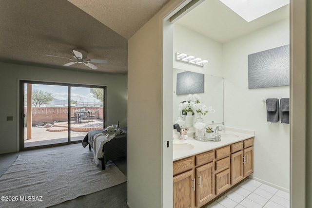 full bathroom featuring a ceiling fan, double vanity, a skylight, a sink, and a textured ceiling