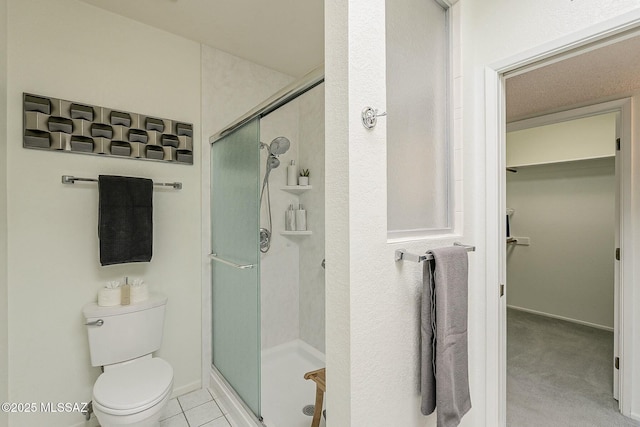 bathroom with tile patterned flooring, a walk in closet, baseboards, toilet, and a stall shower