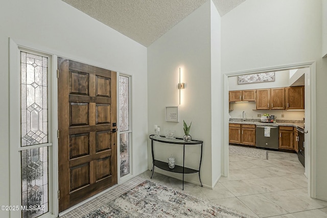 foyer with light tile patterned flooring, high vaulted ceiling, a textured ceiling, and baseboards