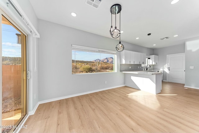 kitchen with light countertops, hanging light fixtures, white cabinets, a sink, and a peninsula