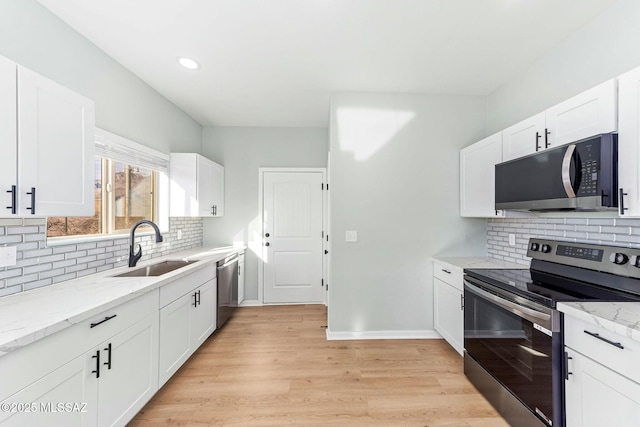 kitchen with light stone counters, stainless steel appliances, a sink, light wood-style floors, and white cabinets