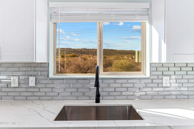 details featuring light stone counters, backsplash, a sink, and white cabinetry