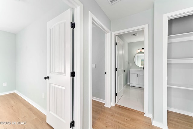 corridor with light wood-type flooring, baseboards, and visible vents