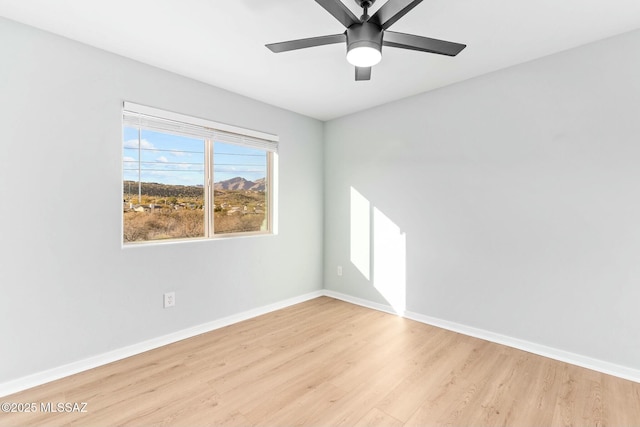 empty room with ceiling fan, light wood finished floors, and baseboards
