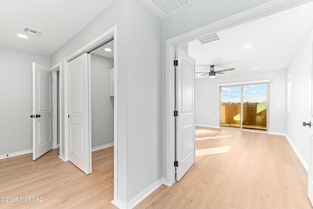 hall featuring light wood-style flooring, visible vents, and baseboards