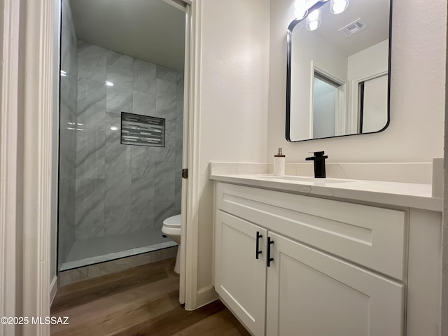 bathroom featuring hardwood / wood-style flooring, vanity, toilet, and a tile shower