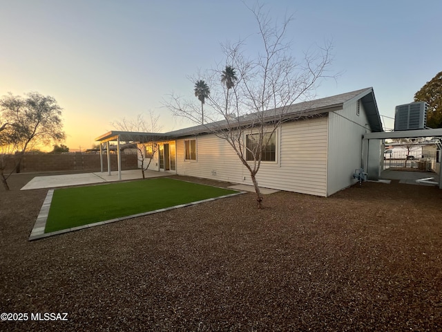 back house at dusk with a yard, central AC, and a patio area