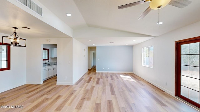 spare room featuring ceiling fan with notable chandelier, vaulted ceiling, and light hardwood / wood-style flooring