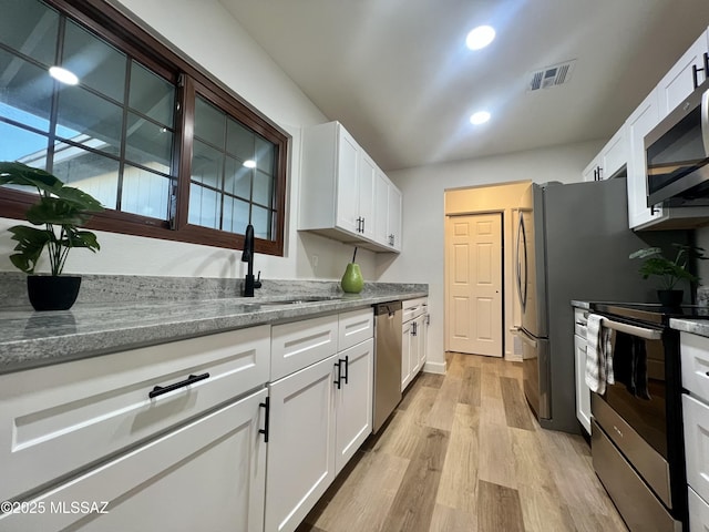 kitchen with stainless steel appliances, sink, white cabinets, and light hardwood / wood-style floors