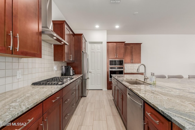 kitchen with wall chimney exhaust hood, sink, stainless steel appliances, light stone countertops, and decorative backsplash