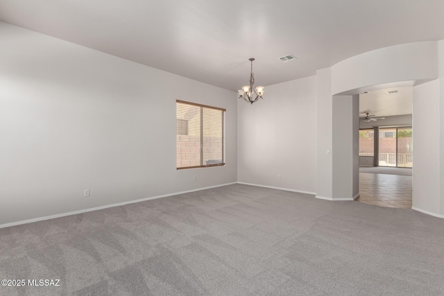 carpeted spare room featuring ceiling fan with notable chandelier