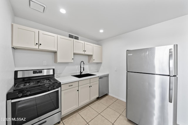 kitchen with appliances with stainless steel finishes, light stone counters, light tile patterned floors, sink, and white cabinetry