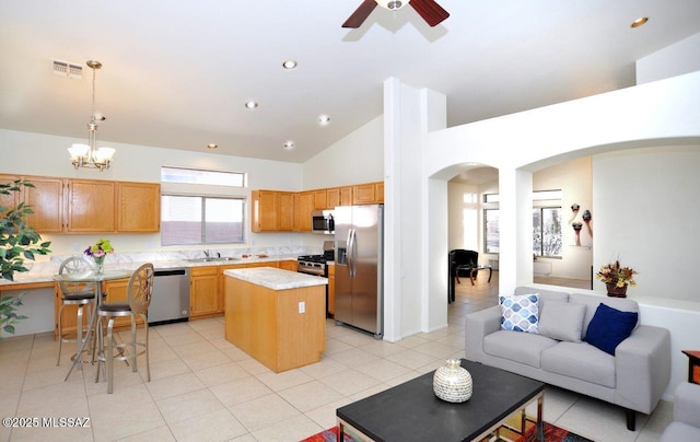 kitchen featuring light tile patterned flooring, a kitchen island, appliances with stainless steel finishes, decorative light fixtures, and sink