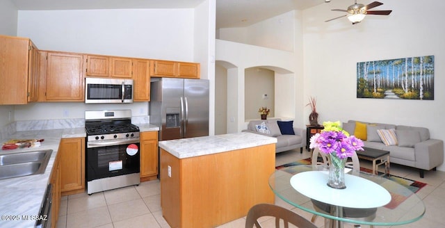 kitchen with a kitchen island, appliances with stainless steel finishes, high vaulted ceiling, light tile patterned floors, and ceiling fan