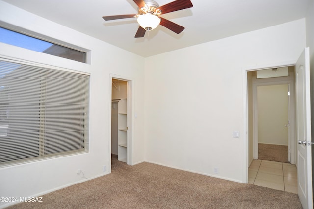 unfurnished bedroom with a walk in closet, light colored carpet, ceiling fan, and a closet