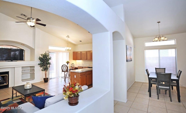 interior space featuring ceiling fan with notable chandelier, a healthy amount of sunlight, light tile patterned floors, and high vaulted ceiling