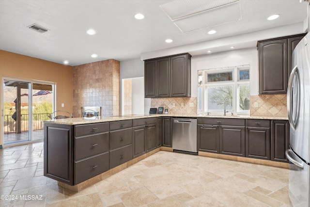 kitchen with a peninsula, a sink, visible vents, appliances with stainless steel finishes, and stone tile flooring