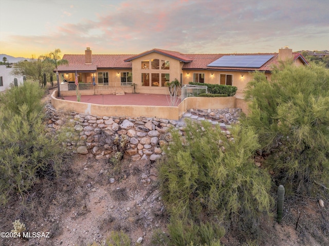 back of house featuring stucco siding, a patio, a chimney, and solar panels