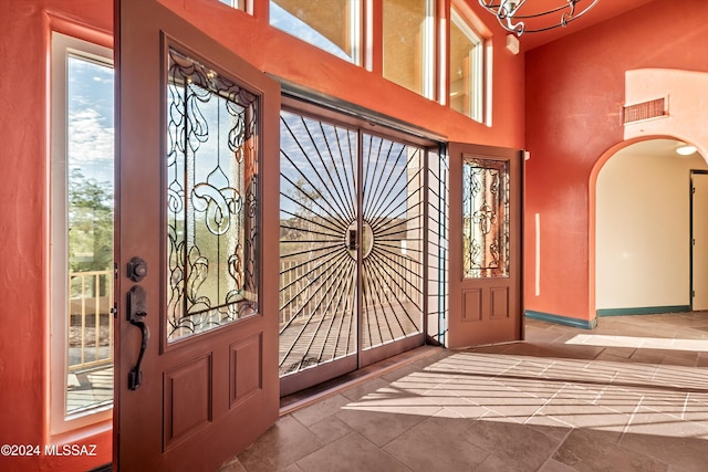 entrance foyer with visible vents, arched walkways, baseboards, a towering ceiling, and stone tile flooring