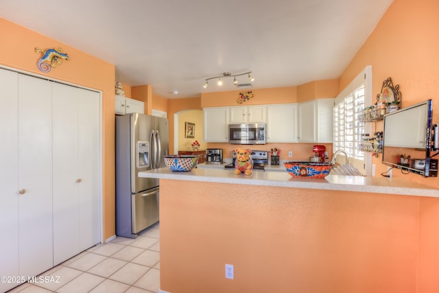 kitchen with light tile patterned floors, stainless steel appliances, kitchen peninsula, and white cabinets