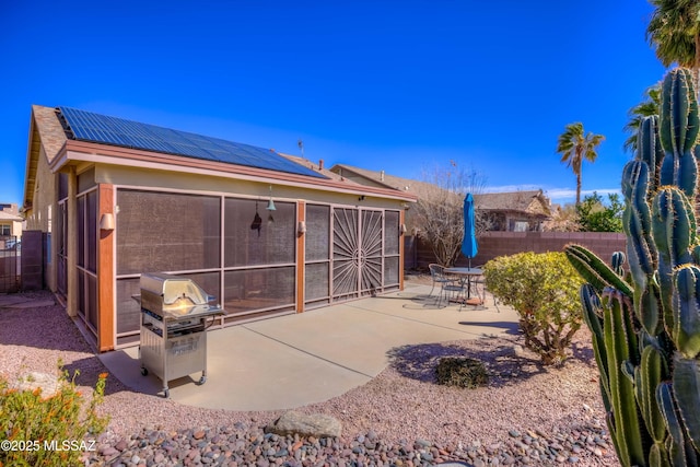 back of property with a sunroom, a patio area, and solar panels